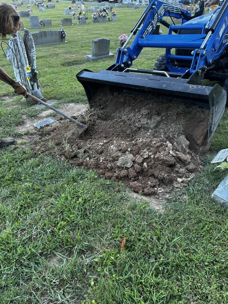 A worker and bulldozer flatten dirt on a fresh grave.